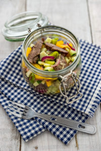 Rindfleischsalat, buntes Gemüse, im Einmachglas auf weißem Holzuntergrund und blauweiß kariertem Tuch, mit Campinggabel Rindfleischsalat, buntes Gemüse, im Einmachglas auf weißem Holzuntergrund und blauweiß kariertem Tuch, mit Campinggabel